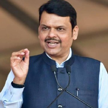 Devendra Fadnavis, Chief Minister of Maharashtra, speaks at a podium while announcing the state's plan to introduce India's first blockchain-based land tokenization law. He is dressed in a traditional white kurta paired with a navy blue vest.
