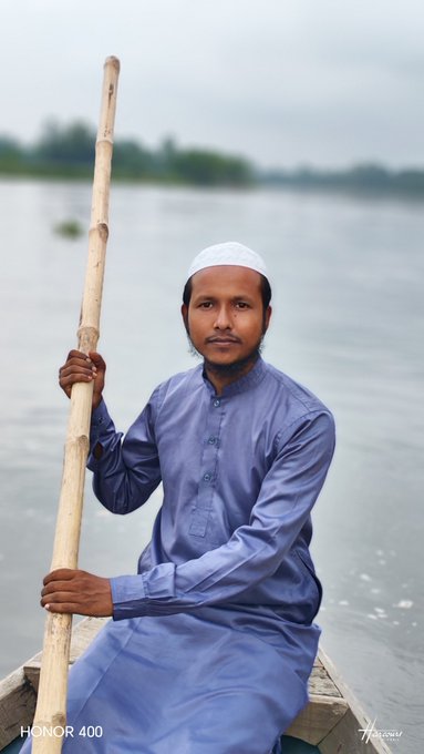 A man in a traditional blue kurta and white prayer cap holds a long wooden pole while seated in a small boat on a calm waterway. The image, watermarked "HONOR 400," appears to be a personal portrait rather than directly illustrating the post about the @NucleusCodes and @EthraShip blockchain/RWA protocol project.