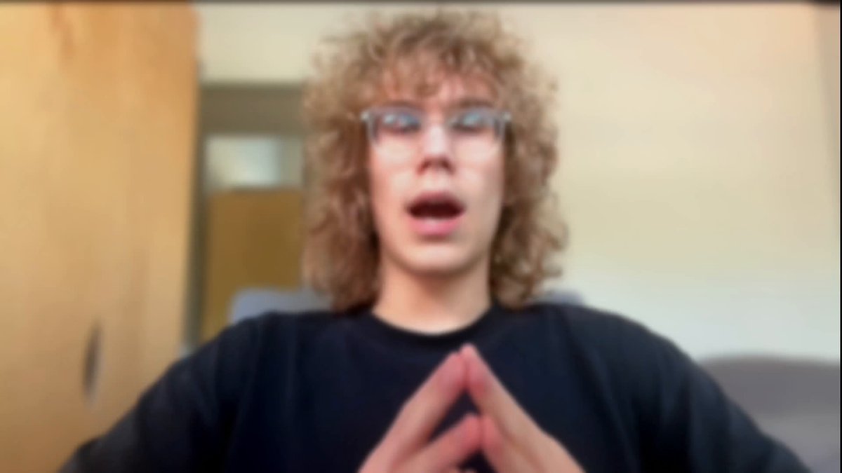 The image shows a person with curly hair wearing glasses making a hand gesture as if they are speaking or giving instructions. The background appears to be a room with a wooden door visible behind them, suggesting that this scene takes place indoors. The caption of the image reads "This is what real-time @HyperliquidX liquidation alerts look like in your Discord Open source, you write the rules, minutes from clone to first ping".