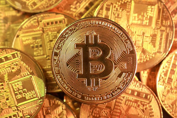 A close-up photograph shows several golden Bitcoin tokens with the iconic 'B' symbol prominently displayed in the center.