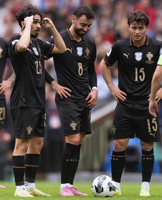 Three soccer players wearing black Portugal national team kits with gold trim stand on a grass field preparing for a set piece; visible jersey numbers include "20," "8," and "15," with a soccer ball positioned on the ground in front of them.