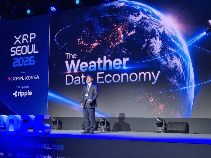 A man in a suit presents on stage at XRP SEOUL 2026, hosted by XRPL KOREA with Ripple as a title sponsor, with a large screen behind him reading "The Weather Data Economy" over an image of the Earth.