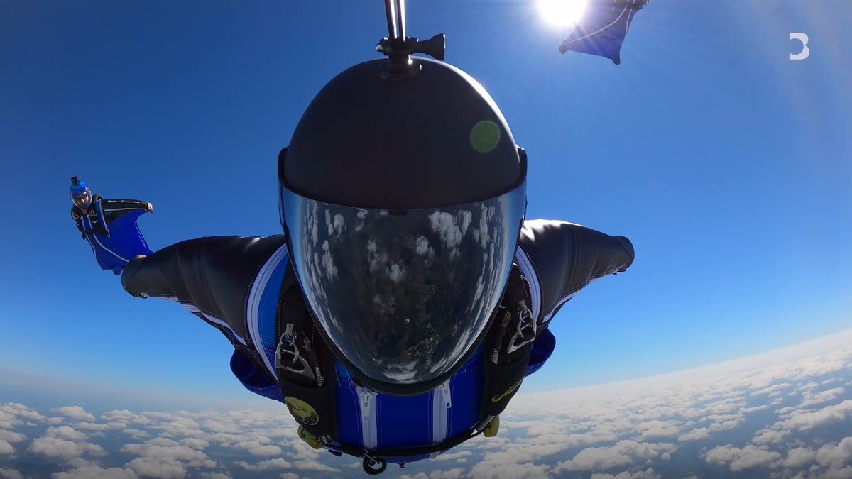 A skydiver soars through the sky above the clouds, wearing a blue and black suit and a reflective helmet that mirrors the landscape below. The image's theme of high-altitude risk-taking parallels the article's description of young investors making risky financial leaps into meme stocks, options, and crypto amid economic instability. A small "B" logo is visible in the upper right corner.