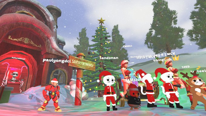 A festive virtual holiday scene shows various avatar characters dressed in Christmas outfits gathered around a decorated tree and a 'Santa's Workshop' sign, with usernames like 'paulyongdci' and 'Sandsman' visible.