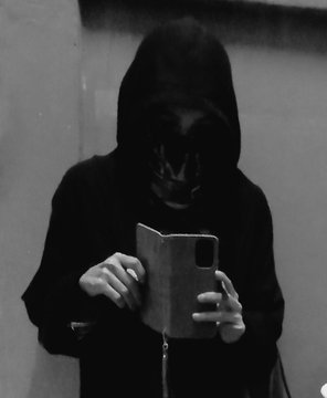 Black-and-white image of a hooded figure looking down at a phone in a dark, shadowy setting.