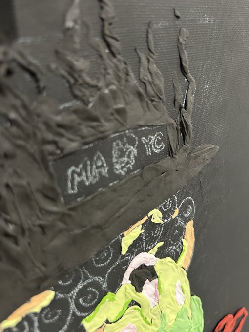 A mixed media artwork in progress showing sculpted black flames above a painted piece with colorful green, yellow, and pink elements.