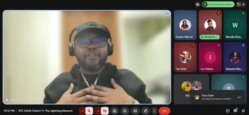 The image shows a man wearing headphones sitting at his computer with a screen displaying a video call from another person. The two individuals are engaged in a conversation, possibly discussing Bitcoin or other financial topics related to the Lightning Network.