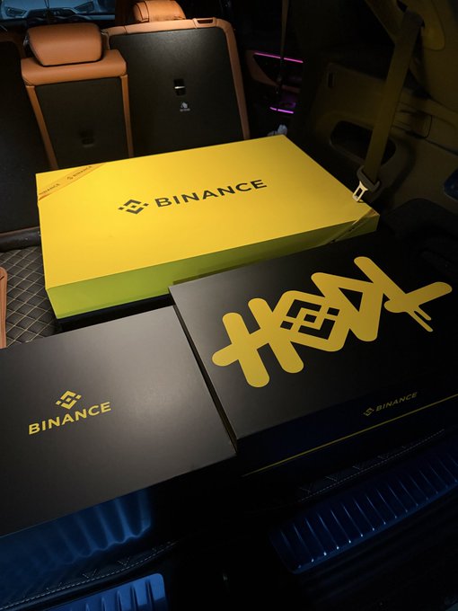 Two Binance boxes and a yellow Binance-branded package sitting in the back seat of a car, along with a black 'HEX' branded item.