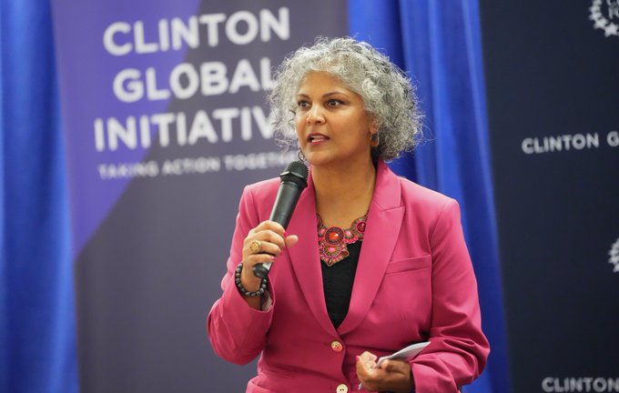 A woman with gray curly hair, wearing a bright pink blazer and statement necklace, speaks into a microphone on stage at the Clinton Global Initiative, with "CLINTON GLOBAL INITIATIVE - TAKING ACTION TOGETHER" visible on the backdrop. The image captures a speaker at the event where Circle Foundation announced its grant to Pacific Community Ventures for the Radiant Data Hub AI platform supporting community lenders.