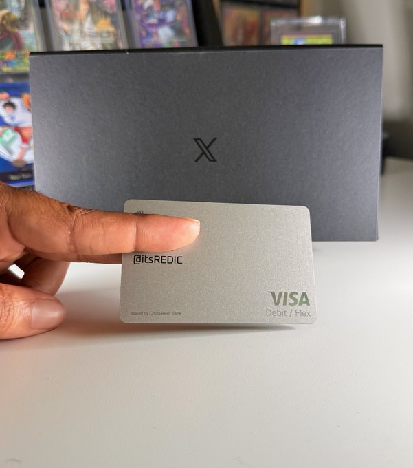 A hand holds up a sleek metallic Visa Debit/Flex "X" card with "@itsREDIC" printed on it, in front of its dark gray branded packaging, showcasing the premium quality card featuring a custom handle—a thoughtful design detail highlighted in the accompanying post.