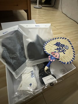 The image shows a white box containing various items, including a fan with a cartoon pig design, a black shirt, and some other clothing items. The text "@Saki_HTX 老师的礼物，感谢 @HuobiGlobal 衣服面料很越扇越火 用手机拍". This post seems to be promoting a fan or clothing items, possibly related to the Saki brand.