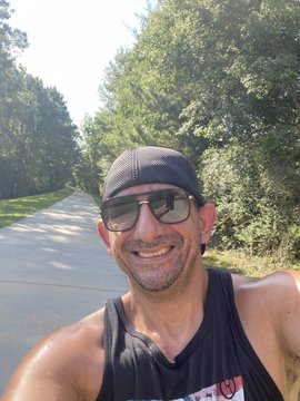 A smiling man in a backwards cap and sunglasses takes a selfie while running on a tree-lined road, visually embodying the post's message about the effort and determination required to win—each step on the open road representing the hard work and commitment to showing up and pushing forward.