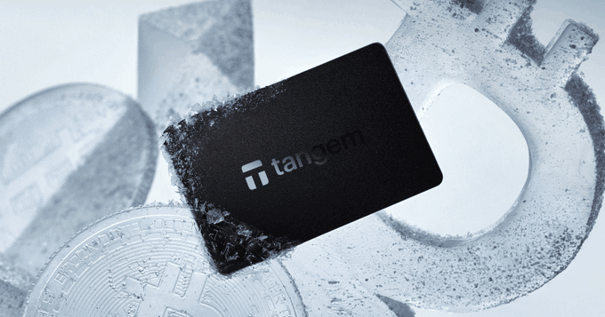 A black Tangem hardware wallet card rests on a frosty surface alongside silver cryptocurrency coins.