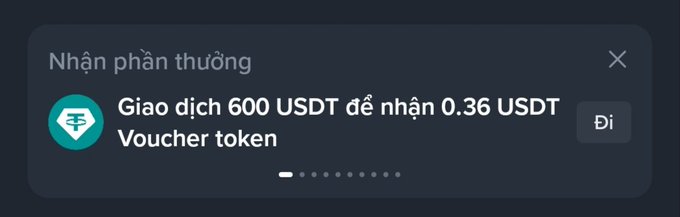 A dark-themed app notification in Vietnamese reads 'Nhận phần thưởng: Giao dịch 600 USDT để nhận 0.36 USDT Voucher token' with a 'Đi' button.