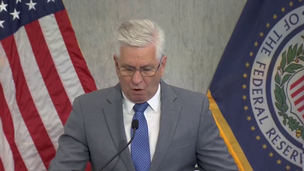 The image features a man wearing glasses, standing at a podium with his hands behind him as he speaks into a microphone. The man appears to be delivering a speech or addressing an audience. In front of the speaker, there are two flags - one representing the United States and another symbolizing the Federal Reserve Bank of New York. The text in the image reads "MASSIVE NEW CHANNEL LINKING GLOBAL LIQUIDITY DEMAND DIRECTLY TO US TreasURY MARKETS!". This suggests that the man's speech could be related to financial matters or the economy, possibly discussing the role of the Federal Reserve Bank of New York and its impact on global liquidity.