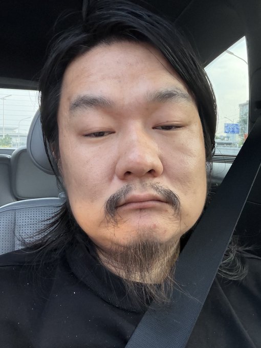 A man with a goatee and long hair takes a selfie in a car, his expression conveying weariness or resignation. The image pairs with his post about the absurdity of feeling comfortable trading massive Ethereum positions but now feeling anxious opening a small 13-share US stock position, capturing the emotional shift between bold crypto trading and cautious stock market investing.