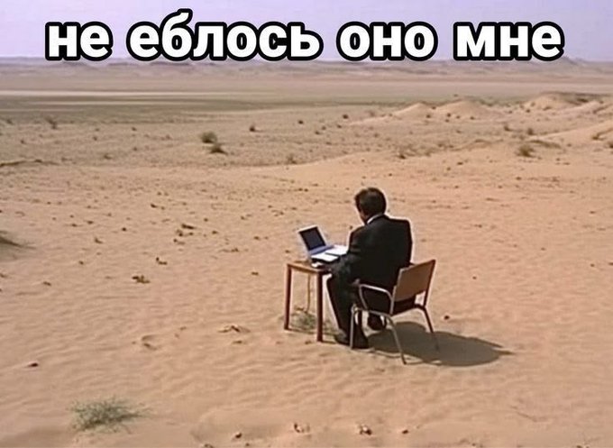 A meme showing a man in a suit sitting at a desk with a laptop in the middle of a desert, overlaid with Russian text 'не еблось оно мне'.