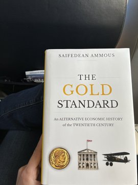 A person holding the book "The Gold Standard: An Alternative Economic History of the Twentieth Century" by Saifedean Ammous.
