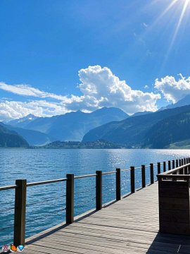 Scenic view of a wooden pier extending into a calm blue lake with mountains and a cloudy sky in the background.