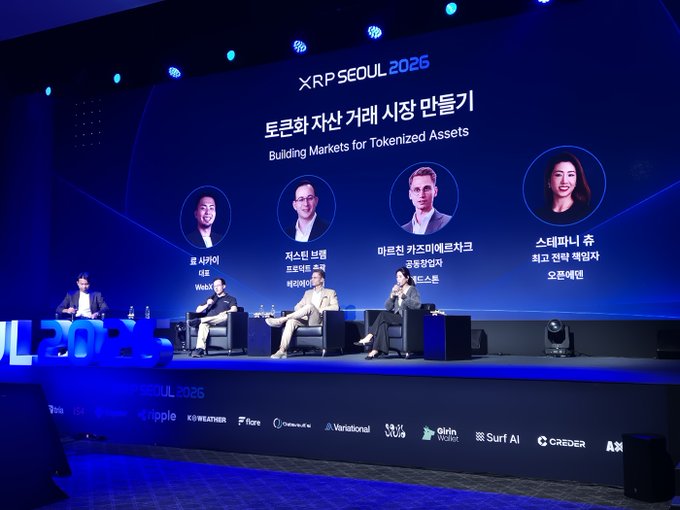 A panel discussion at 'XRP SEOUL 2025' on 'Building Markets for Tokenized Assets' featuring four speakers seated on stage with their photos and names displayed on the screen.