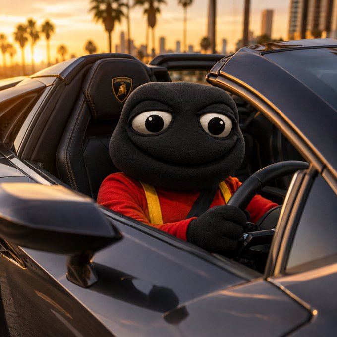 A black puppet character wearing a red and yellow racing suit drives a black Lamborghini with the Lamborghini logo on the seat, set against a sunset cityscape with palm trees.