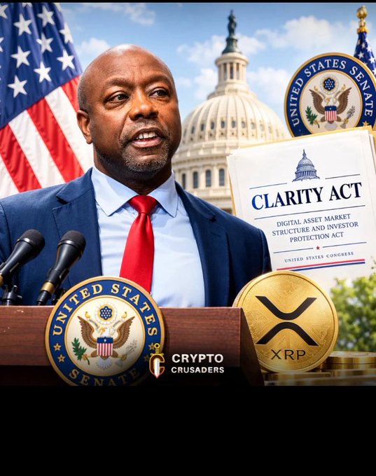 A man in a suit with a red tie speaks at a podium bearing the United States Senate seal, with a document titled 'CLARITY ACT - DIGITAL ASSET MARKET STRUCTURE AND INVESTOR PROTECTION ACT' and an XRP coin visible, branded by 'Crypto Crusaders'.