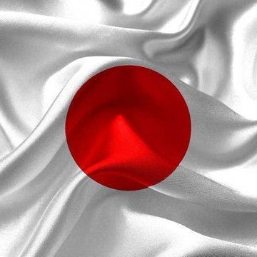 A silken white flag with a red circle in the center, the national flag of Japan, displayed with rippling folds.