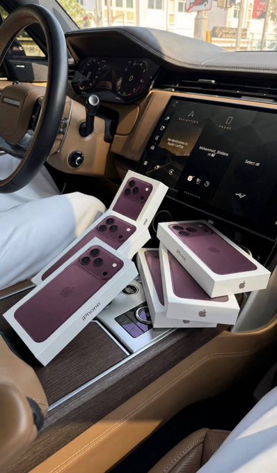 Six sealed "iPhone" boxes are stacked on the center console of a luxury car featuring a tan leather interior and digital dashboard, visually supporting the "6 iPhone 18 Pro Max" giveaway claim, though the boxes suspiciously appear to show older iPhone Pro model designs rather than the announced "iPhone 18 Pro Max."