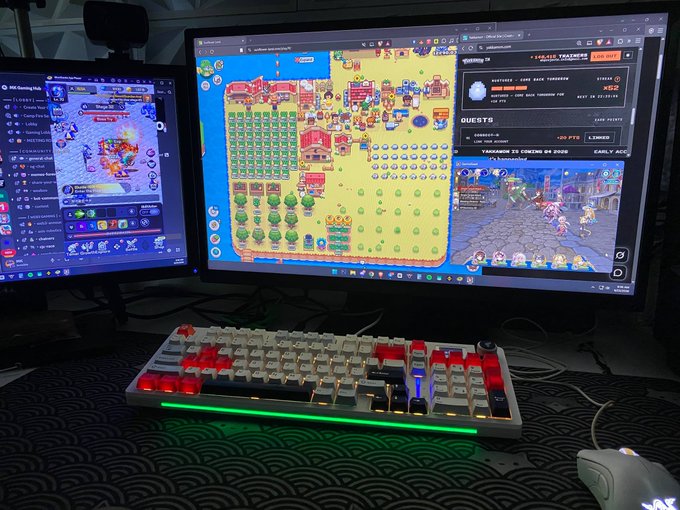 Gaming setup with two monitors, the right displaying an idle game, and a mechanical keyboard with red and white keycaps and green RGB lighting on the desk.