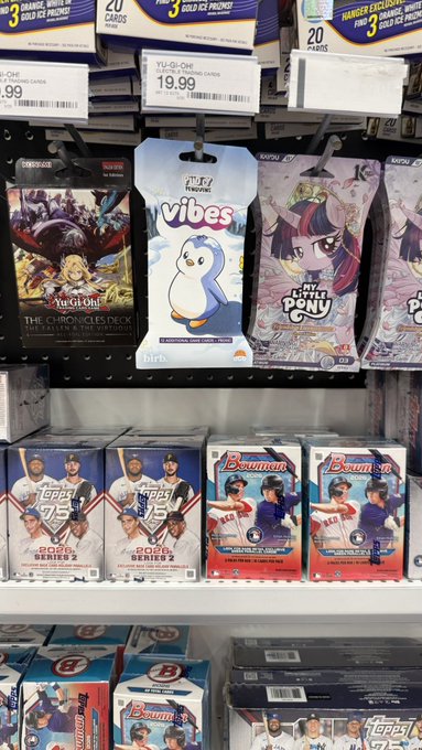 A store shelf displaying various trading card game products including Yu-Gi-One!, Vibes (Feeding Frenzie), My Little Pony, Topps 2025 Series 2, and Bowman.