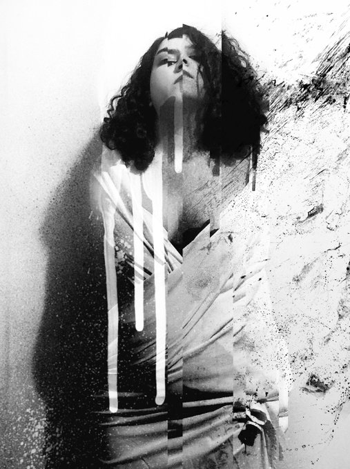 The image features an artist's portrait of a woman with curly hair, wearing a dress that has white lines running through it. The photo appears to be black and white, giving it a timeless quality. The woman is positioned centrally within the frame, drawing attention to her face as she looks up at something above her head. The background is blurred, making it difficult to discern any details beyond what's directly in front of the woman. The image also contains text that reads "GM Interwined" and "@janisour33 6 ed." This suggests that the photo may be part of a larger collection or series by the artist.