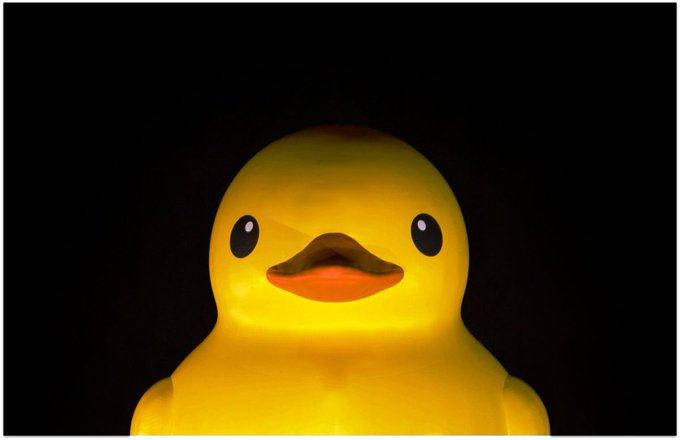 A close-up photograph of a glowing yellow rubber duck against a black background.