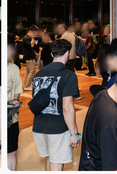 A man with a black crossbody bag stands in the foreground of a crowded networking event, viewed from behind in a black T-shirt and beige shorts. The post identifies him as attending the Hyperliquid event during Singapore Token 2049 and appearing on hyperliquid.xyz/about.