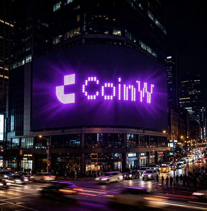 A nighttime cityscape features a large illuminated billboard displaying the word 'coiny' in bright purple letters on the side of a building at a busy intersection.