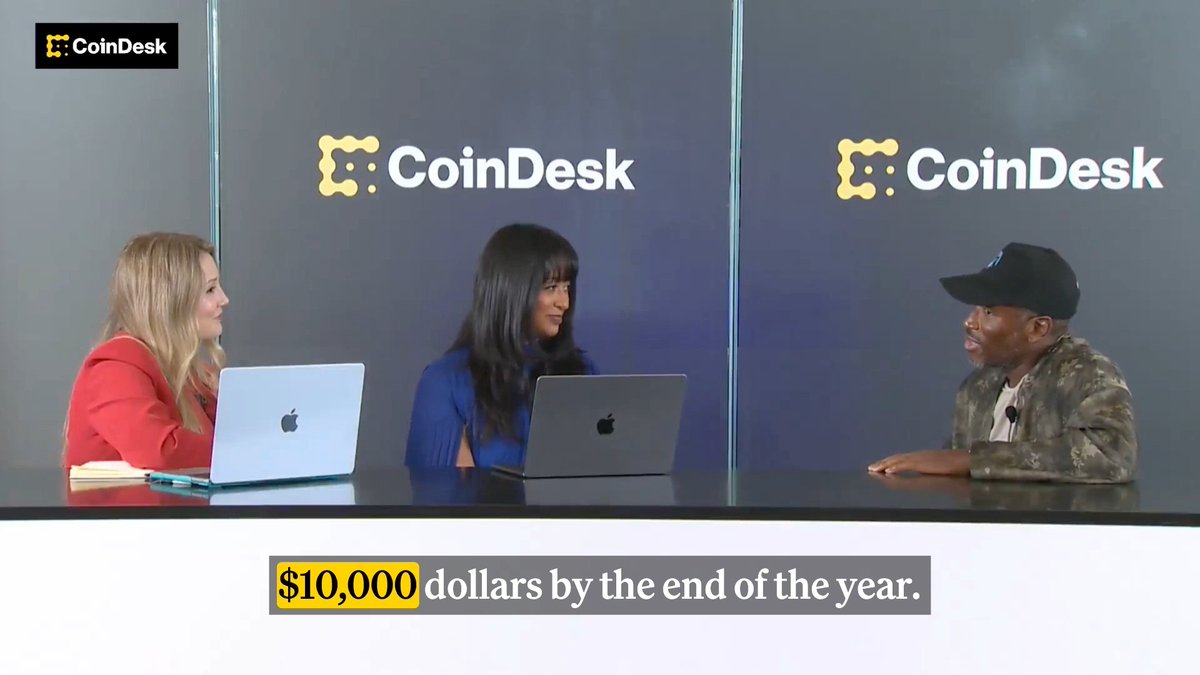 Crypto influencer Arthur Hayes sits at a CoinDesk interview desk with two female hosts, making a bullish prediction of $10,000 ETH by year's end, as displayed in the caption overlay. The branded CoinDesk backdrop and MacBooks on the desk reinforce the professional media setting for this crypto price forecast discussion.