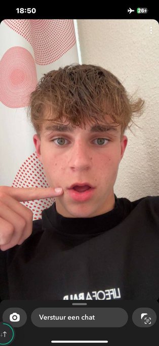 A young man with light brown hair pointing at his cheek during a TikTok live stream, with 'Verstuur een chat' visible at the bottom.