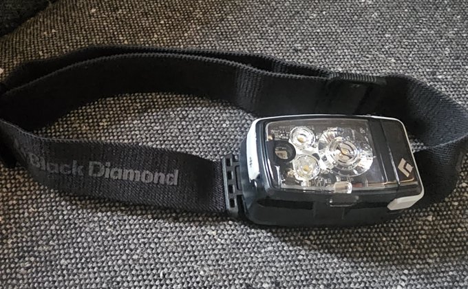 A fully charged Black Diamond headlamp rests on a textured gray surface, ready for an upcoming adventure into the higher elevations.