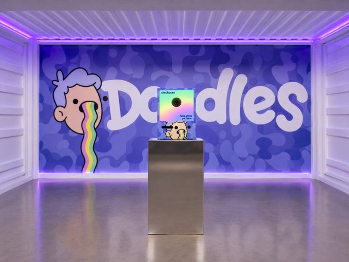 A Doodles NFT display at Summer House LA features a vibrant exhibit with the signature Doodles logo and rainbow-stream character mural, set against purple LED-lit walls for the Solana-sponsored "come get doodled" event.