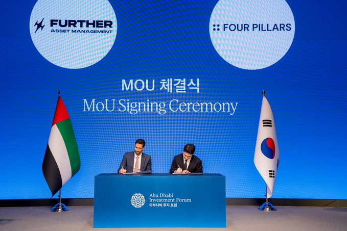 Two men sign documents at a blue-draped table during an MoU Signing Ceremony between Further Asset Management and Four Pillars at the Abu Dhabi Investment Forum, flanked by UAE and South Korean flags.