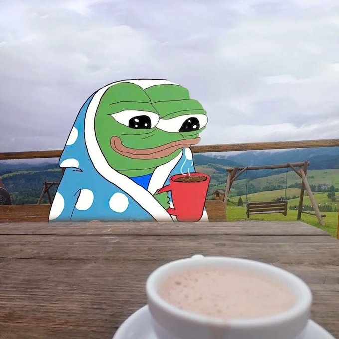 A Pepe the Frog meme character wearing a polka-dot robe sits at a wooden table outdoors, holding a steaming red mug while a creamy beverage sits in the foreground, fitting the relaxed "gm" (good morning) crypto greeting vibe of starting a new week.