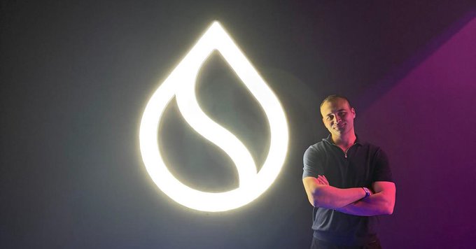 Photo of a man standing next to a glowing neon drop/flame logo.