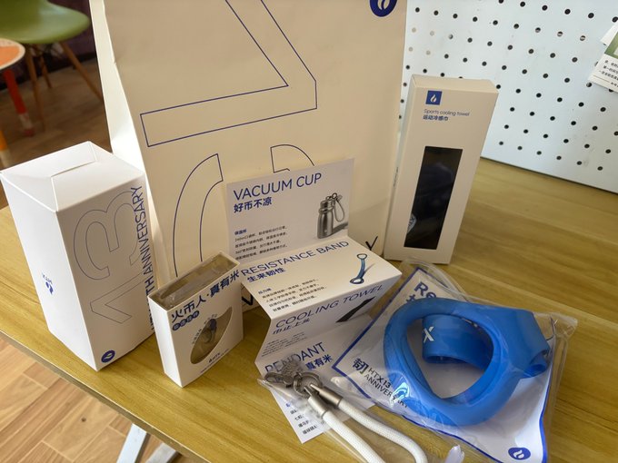 A display of products on a wooden shelf including a vacuum cup, sports cooling towel, resistance band, and toothbrush set, with Chinese labels like '好市不累' and '运动冷感巾' alongside a 10th Anniversary branded box.
