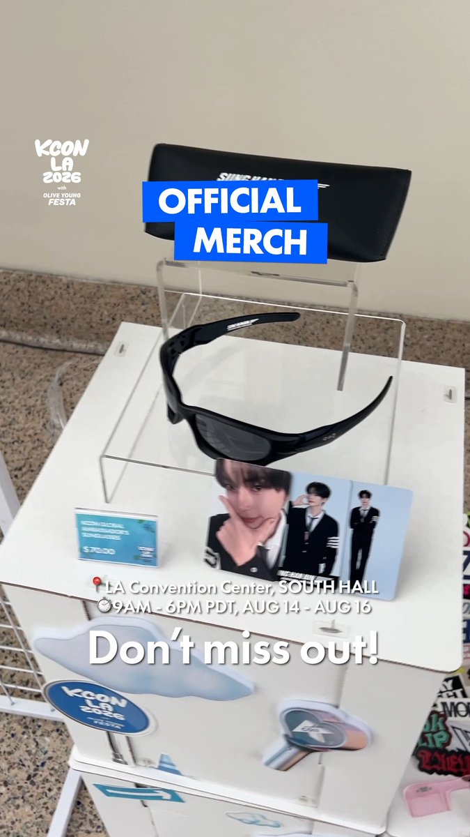KCON LA 2026 official merchandise display featuring custom sunglasses, photocard, and accessories at the LA Convention Center South Hall, with on-site sales running 9AM-6PM PDT, August 14-16.