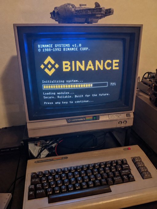 A vintage Commodore monitor and keyboard display a retro-styled "BINANCE SYSTEMS v1.0" boot screen with an initialization progress bar at 72%, cleverly reimagining the modern Binance crypto exchange as if it were an 8-bit computer system from 1988-1992.