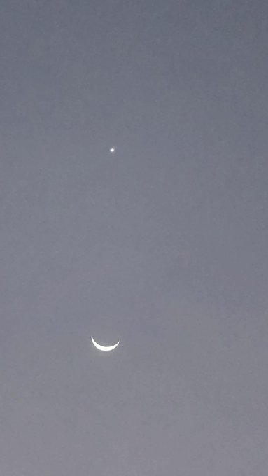 A photograph of a dusky blue-grey sky showing a bright point of light (likely Venus) above a crescent moon.