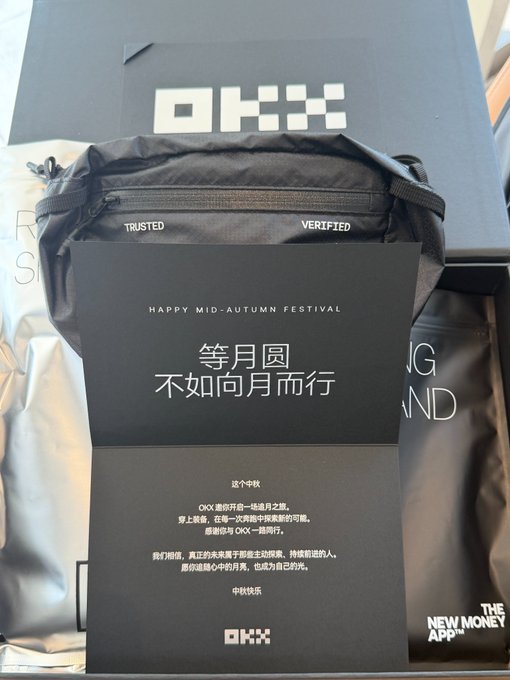 An OKX-branded Mid-Autumn Festival gift box featuring a sleek black waist bag with "TRUSTED" and "VERIFIED" accents, accompanied by a card reading "等月圆 不如向月而行" with the English theme "Don't wait for the moon, run to it." The packaging also displays "HAPPY MID-AUTUMN FESTIVAL" and the OKX logo, reflecting the thoughtful corporate gift highlighted in the post.
