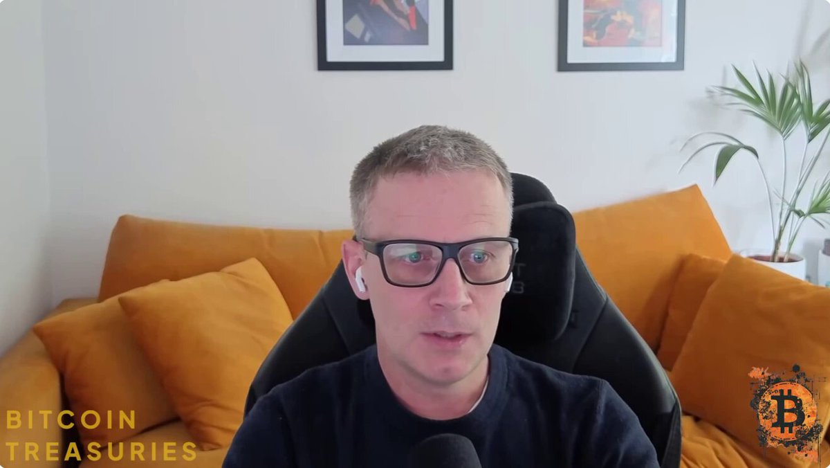 The image shows a man wearing glasses sitting in an office chair, with a couch visible behind him. The man appears to be talking into a microphone or headset while seated at his desk. There are two potted plants in the room - one on the left side and another on the right side of the scene. A computer monitor is also present in front of the man's desk.

The image has a caption that reads "Just In: The Smarter Web Company Andrew Webley just said, 'We want to buy as much Bitcoin as we can at this level without undue stress on the balance sheet.'" This suggests that there might be an ongoing discussion or interview about Bitcoin and its potential impact on the financial world.