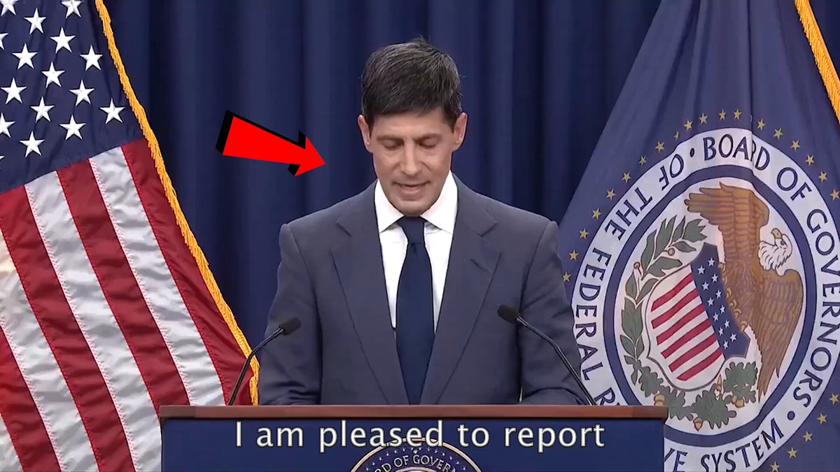 The image shows a man standing at a podium, giving a speech or presentation. The background features an American flag with stars and stripes, as well as a banner that says "I am pleased to report" along with some text. The main focus of the image is on the man speaking at the podium, which suggests he might be discussing a topic related to politics or government.