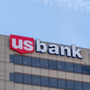The image shows a U.S. Bank logo displayed prominently on the upper facade of a modern building with reflective glass windows against a blue sky. This visual ties directly to the announcement that U.S. Bank successfully executed a live cross-border transfer of its USBDC stablecoin between North American and European entities on the Stellar blockchain, highlighting the bank's expansion into digital currency services.