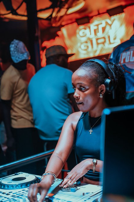 A female DJ wearing headphones operates a mixing console at an event with 'GIFTY GIRL' signage in the background, credited to @melvinnjr_photography.
